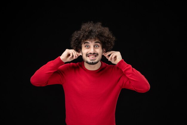 Vue de face du jeune homme en pull rouge sur le mur noir