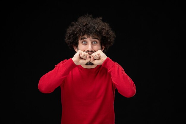 Vue de face du jeune homme en pull rouge sur le mur noir