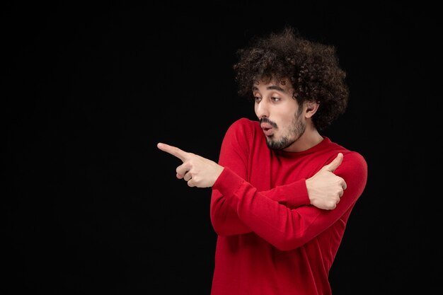 Vue de face du jeune homme en pull rouge sur le mur noir