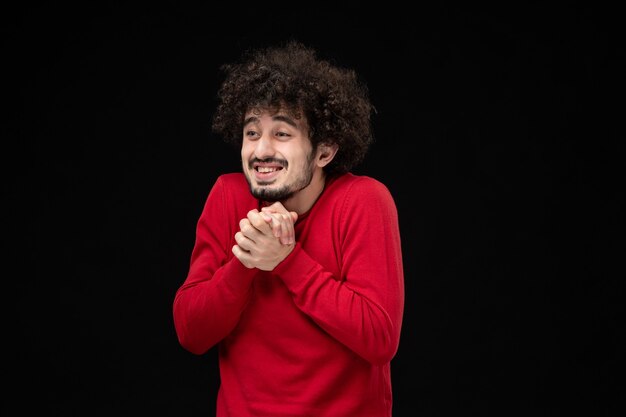 Vue de face du jeune homme en pull rouge sur le mur noir