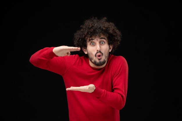 Vue de face du jeune homme en pull rouge sur le mur noir