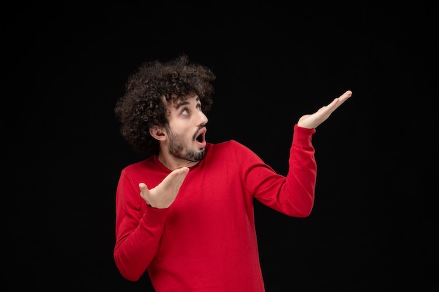 Vue de face du jeune homme en pull rouge sur le mur noir