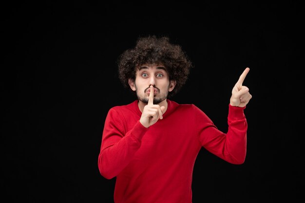 Vue de face du jeune homme en pull rouge sur le mur noir