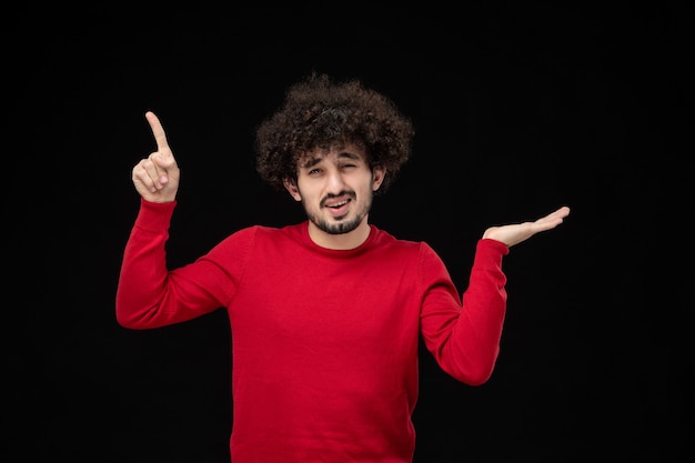 Vue de face du jeune homme en pull rouge sur le mur noir