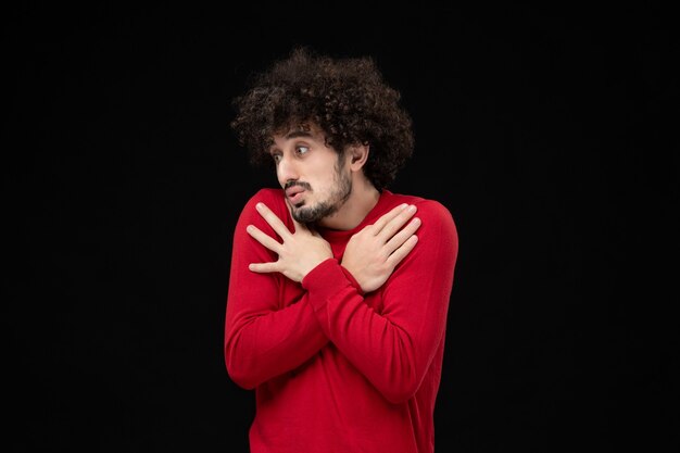 Vue de face du jeune homme en pull rouge sur le mur noir