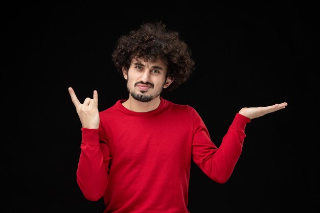 Vue de face du jeune homme en pull rouge sur le mur noir