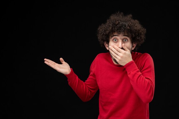 Vue de face du jeune homme en pull rouge sur le mur noir