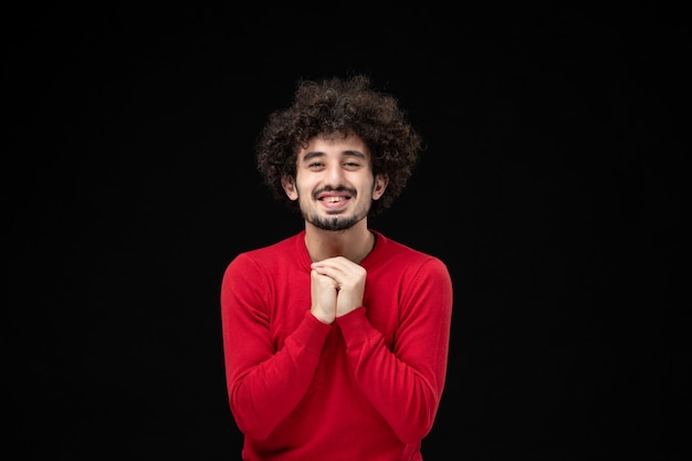 Vue de face du jeune homme en pull rouge souriant sur mur noir