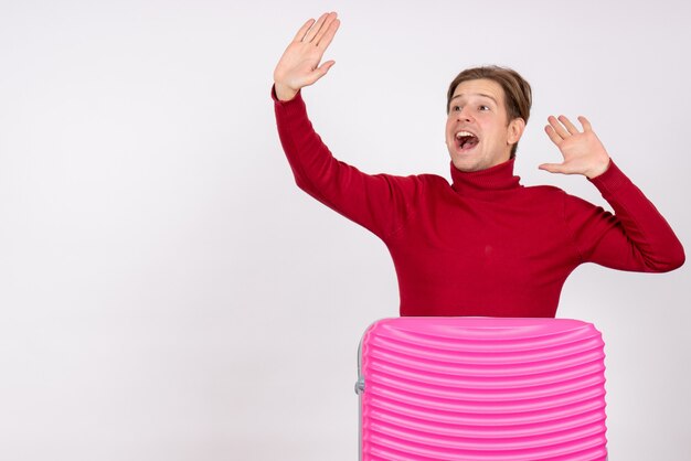 Vue de face du jeune homme avec sac rose sur un mur blanc