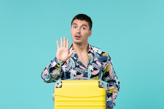 Vue de face du jeune homme se préparant pour les vacances avec sac jaune sur mur bleu