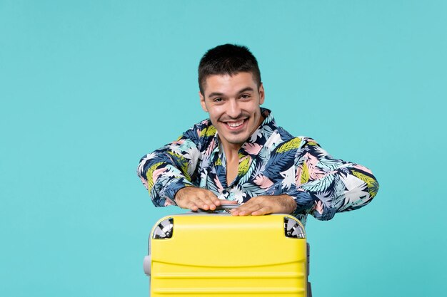 Vue de face du jeune homme se préparant pour le voyage avec son sac jaune sur le mur bleu