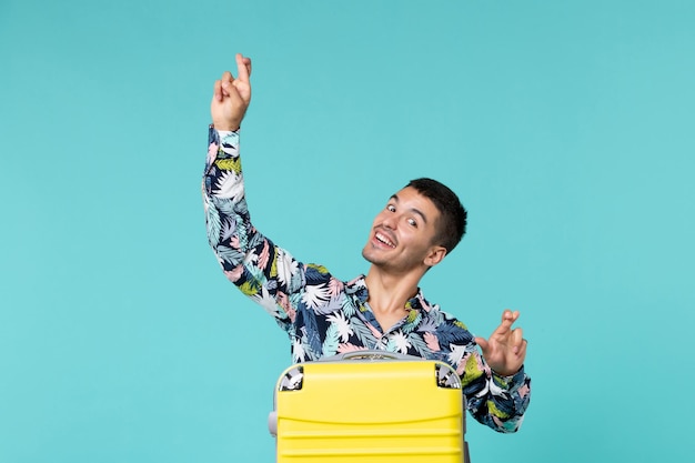 Vue de face du jeune homme se préparant pour le voyage avec son sac jaune sur le mur bleu