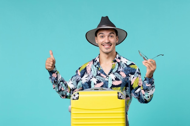 Vue de face du jeune homme avec son sac jaune se préparant pour un long voyage sur le mur bleu