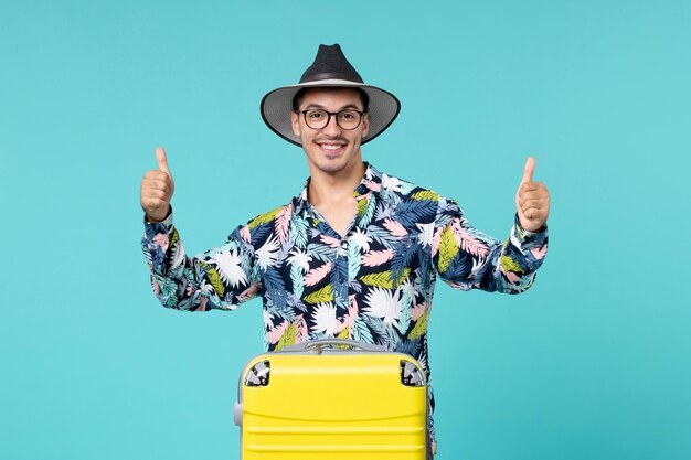 Vue de face du jeune homme avec son sac jaune se préparant pour un voyage sur un mur bleu clair