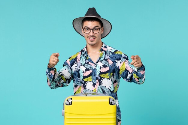 Vue de face du jeune homme avec son sac jaune se préparant pour le voyage sur le mur bleu