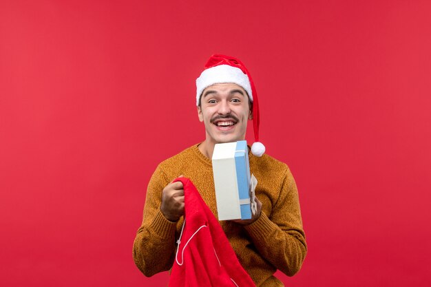 Vue de face du jeune homme sortant des cadeaux du sac sur le mur rouge