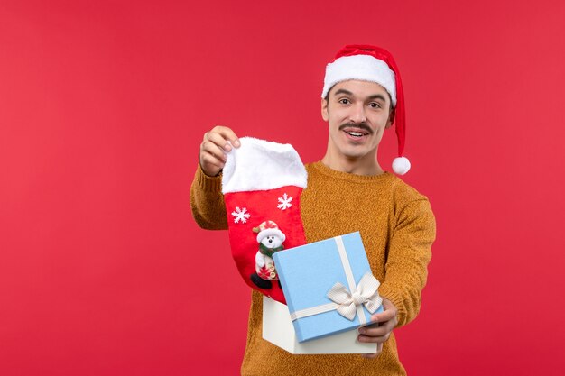 Vue de face du jeune homme sortant la chaussette de Noël sur le mur rouge