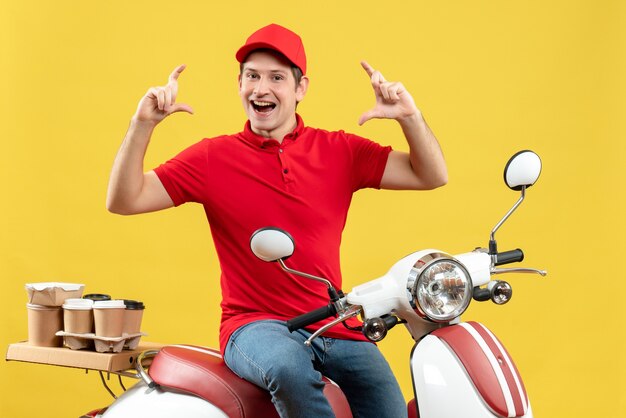 Vue de face du jeune homme souriant portant un chemisier rouge et un chapeau livrant des commandes faisant quelque chose d'exact sur fond jaune