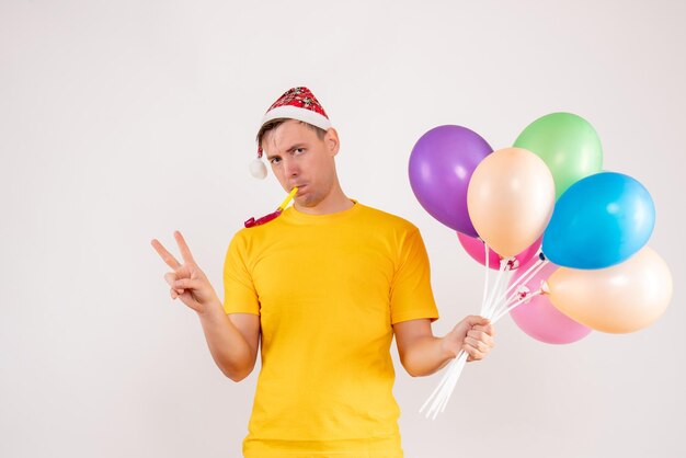 Vue de face du jeune homme tenant des ballons colorés sur un mur blanc