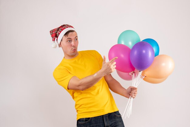 Vue de face du jeune homme tenant des ballons colorés sur un mur blanc