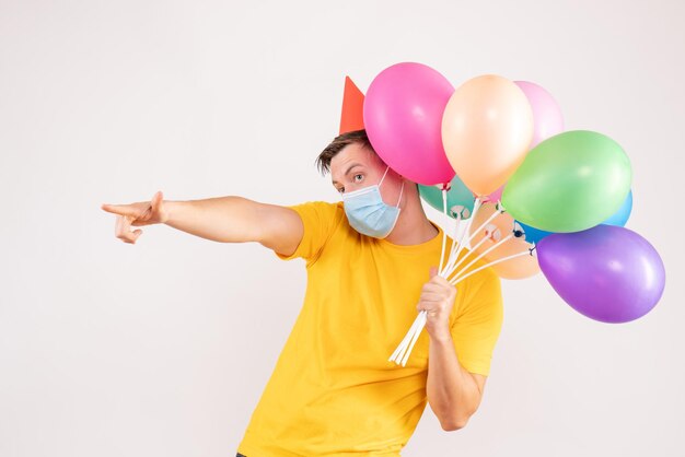 Vue de face du jeune homme tenant des ballons colorés sur un mur blanc