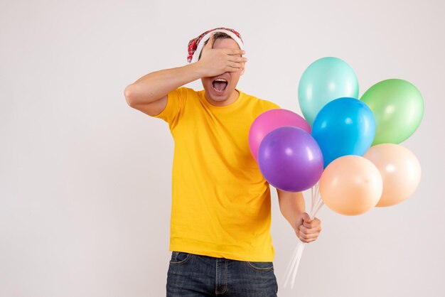 Vue de face du jeune homme tenant des ballons colorés sur un mur blanc