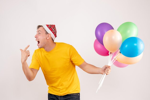 Vue de face du jeune homme tenant des ballons colorés sur un mur blanc