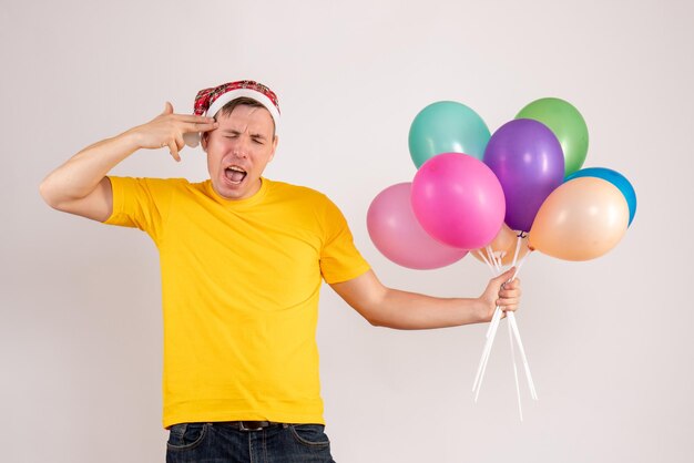 Vue de face du jeune homme tenant des ballons colorés sur un mur blanc