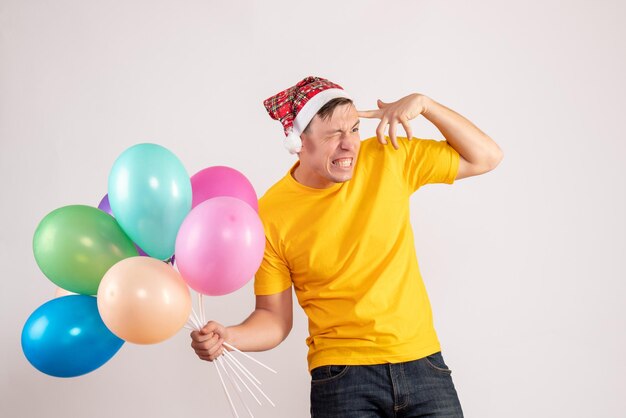 Vue de face du jeune homme tenant des ballons colorés sur un mur blanc