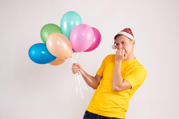 Vue de face du jeune homme tenant des ballons colorés sur un mur blanc