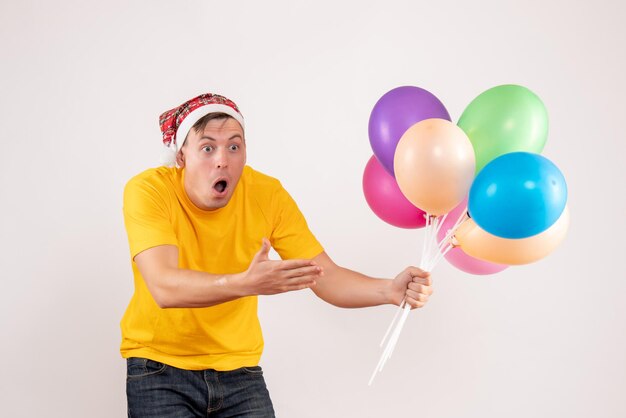 Vue de face du jeune homme tenant des ballons colorés sur un mur blanc