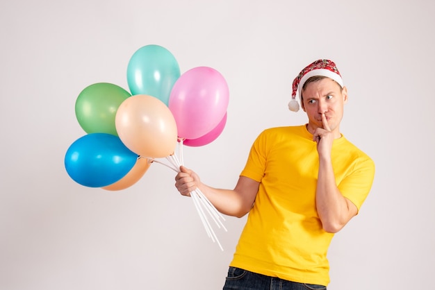 Vue de face du jeune homme tenant des ballons colorés sur un mur blanc