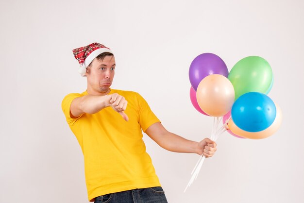 Vue de face du jeune homme tenant des ballons colorés sur un mur blanc