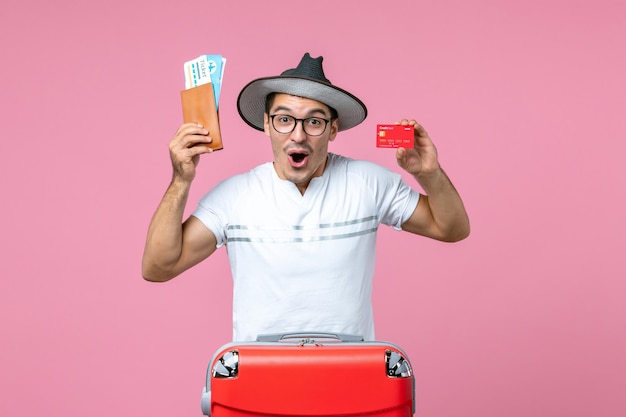 Vue de face du jeune homme tenant des billets et une carte bancaire sur un mur rose clair