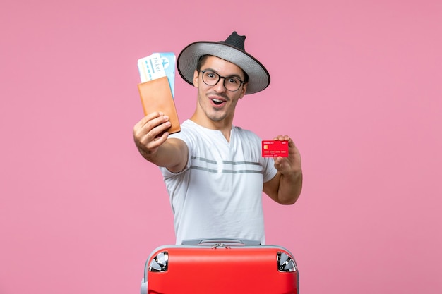 Vue de face du jeune homme tenant des billets et une carte bancaire sur le mur rose