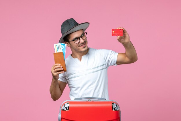 Vue de face du jeune homme tenant des billets et une carte bancaire sur le mur rose