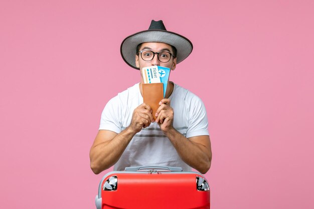 Vue de face du jeune homme tenant des billets de vacances sur le mur rose