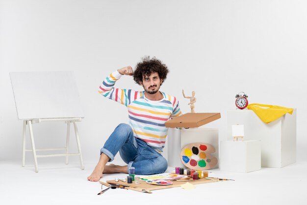 Vue de face du jeune homme tenant une boîte à pizza sur un mur blanc