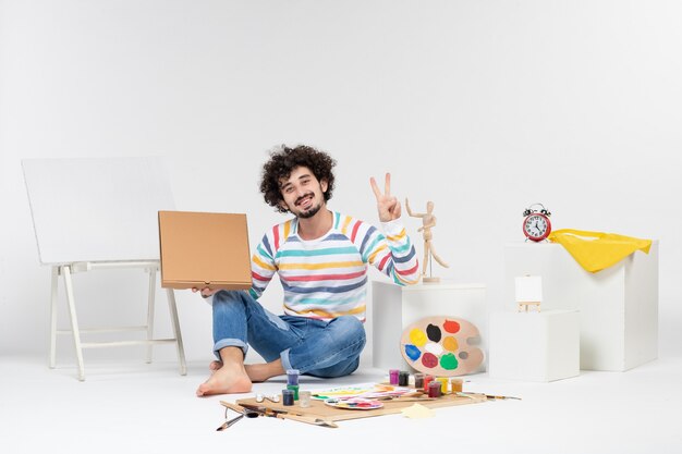 Vue de face du jeune homme tenant une boîte à pizza sur un mur blanc