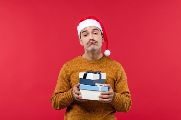 Vue de face du jeune homme tenant des boîtes présentes sur le mur rouge