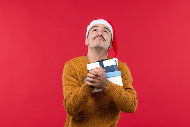 Vue de face du jeune homme tenant des boîtes présentes priant sur un mur rouge