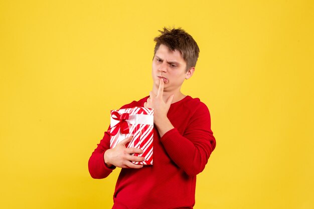 Vue de face du jeune homme tenant le cadeau de Noël confus sur mur jaune