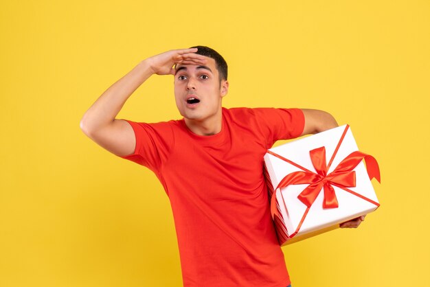 Vue de face du jeune homme tenant le cadeau de Noël sur le mur jaune