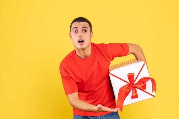 Vue de face du jeune homme tenant le cadeau de Noël sur le mur jaune