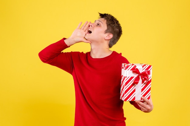 Photo gratuite vue de face du jeune homme tenant le cadeau de noël sur le mur jaune