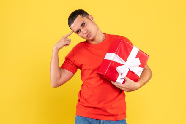 Vue de face du jeune homme tenant le cadeau de Noël sur le mur jaune