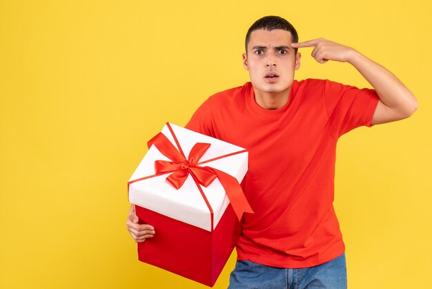 Vue de face du jeune homme tenant le cadeau de Noël sur le mur jaune