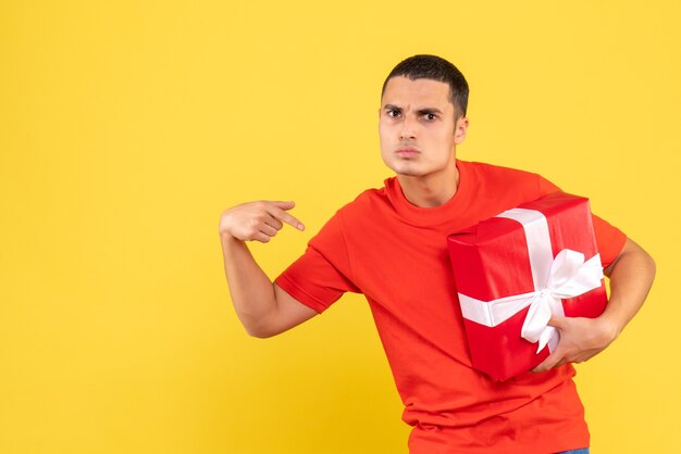 Vue de face du jeune homme tenant le cadeau de Noël sur le mur jaune