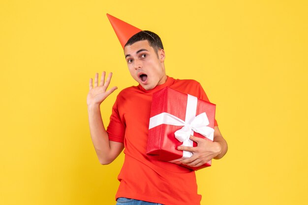 Vue de face du jeune homme tenant le cadeau de Noël sur le mur jaune