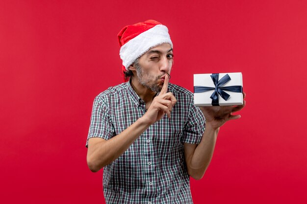 Vue de face du jeune homme tenant un cadeau de Noël sur rouge